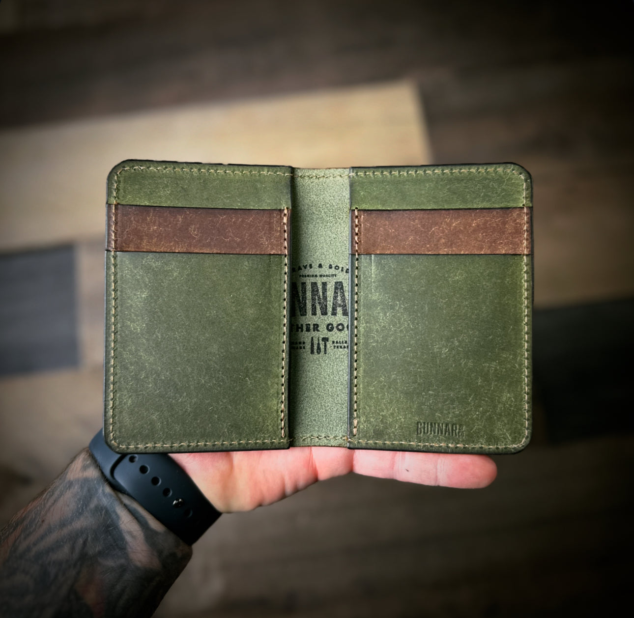 hand holding open two-tone leather wallet - olive green with walnut accents, featuring Gunnar & CO logo and full-grain texture