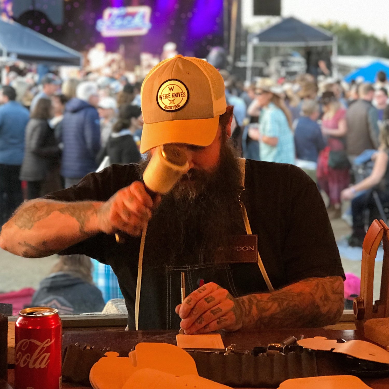 Brandon Pangle of Gunnar & Co. live-stamping leather key fobs at an outdoor event, surrounded by a crowd. Showcasing on-site leather craftsmanship and brand engagement.