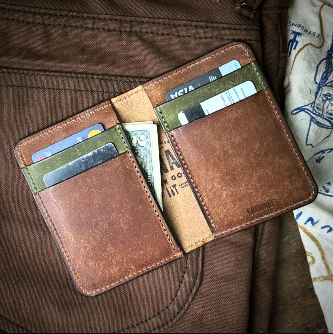 open Two -tone leather wallet on brown canvas pants - showcasing card slots, faded cash, and handcrafted stitching