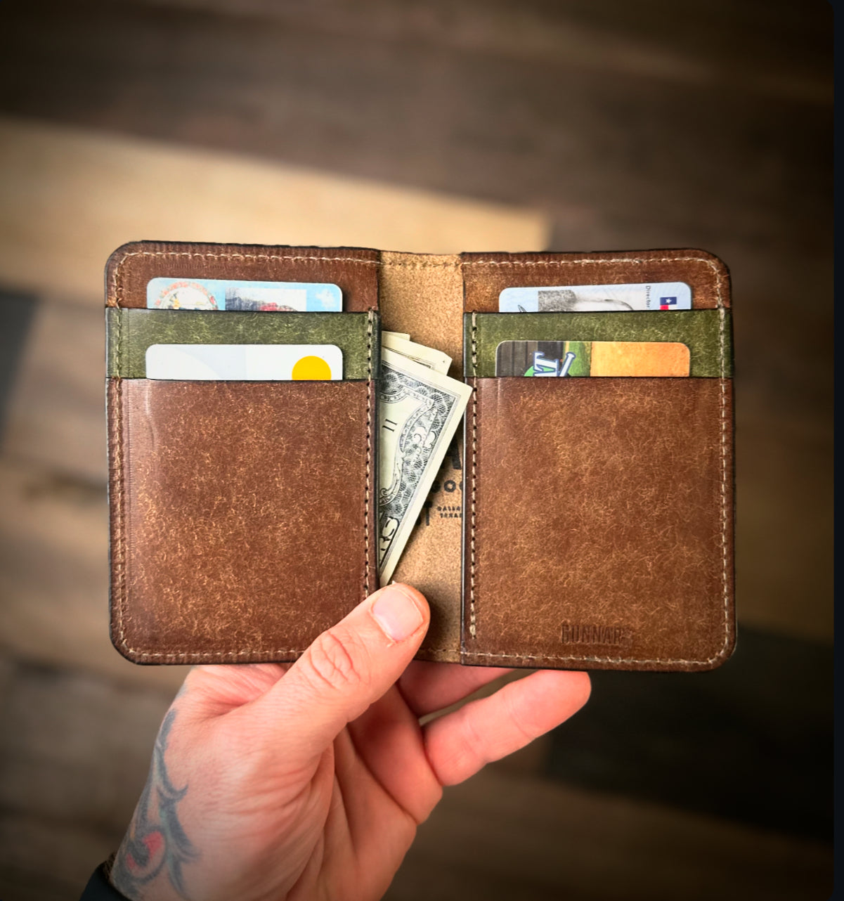 hand holding open brown leather wallet with green accents - filled with cards and folded cash, handcrafted by Gunnar & Co.