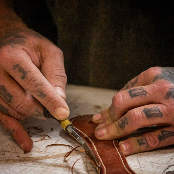 close up of tattooed hands edge beveling leather at Gunnar & CO. workshop