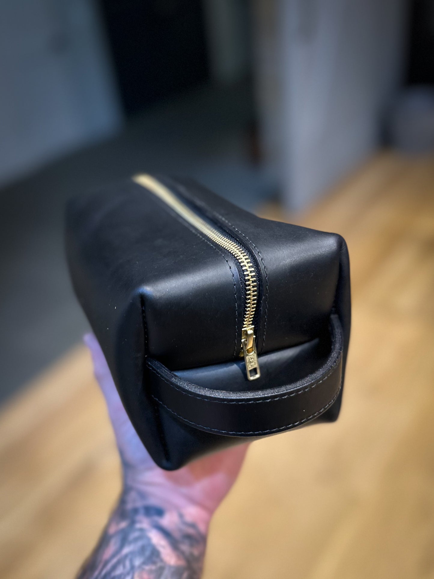 Black leather Dopp kit with gold zipper, captured at an angle to show both top and side profile.