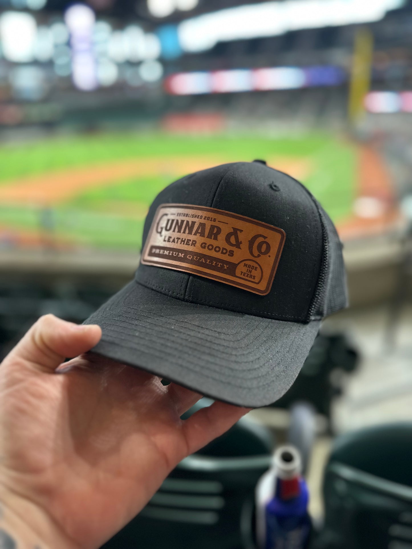 Gunnar & Co. leather patch hat held in hand with baseball field in background