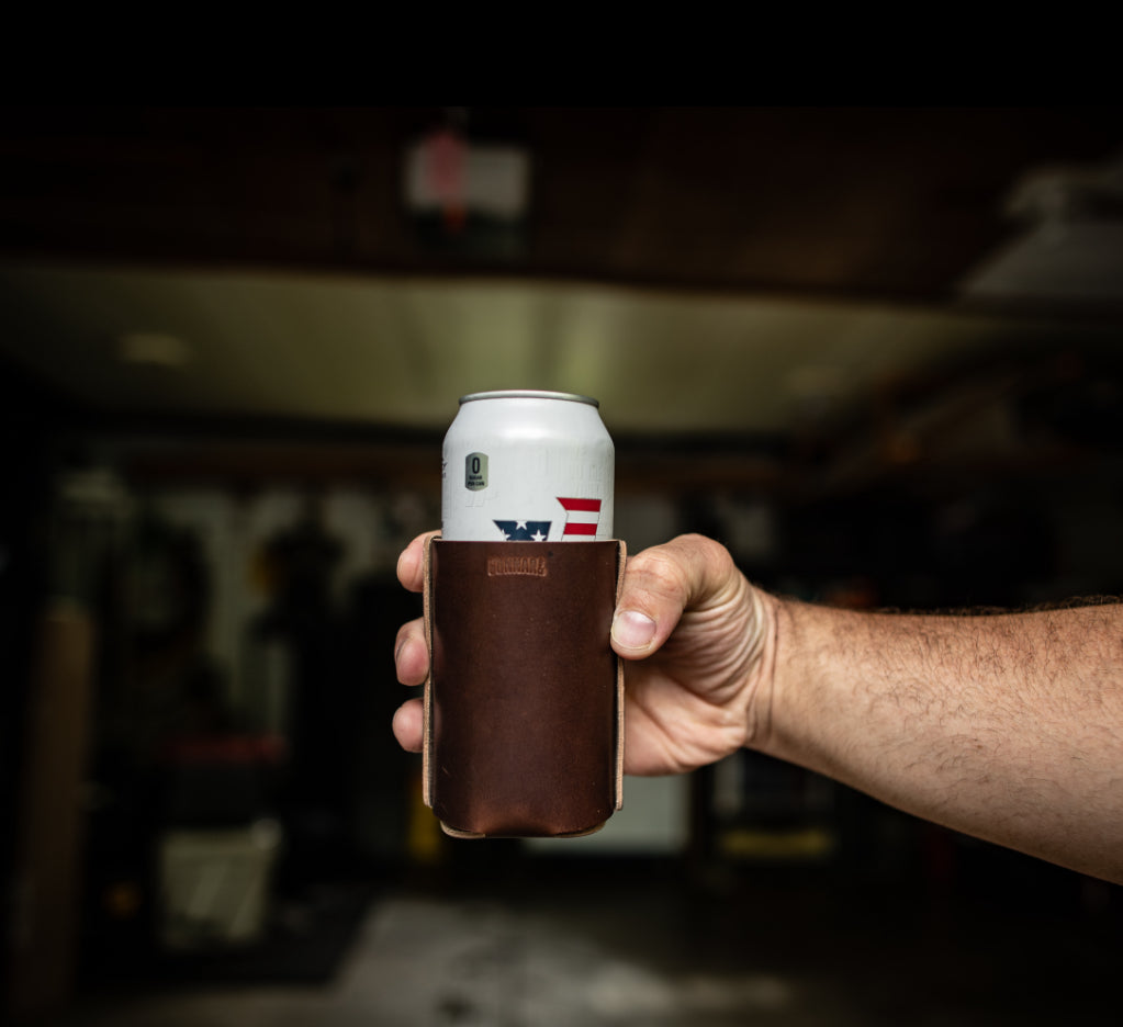 Hand holding brown leather can wrap with a can, blurred workshop background