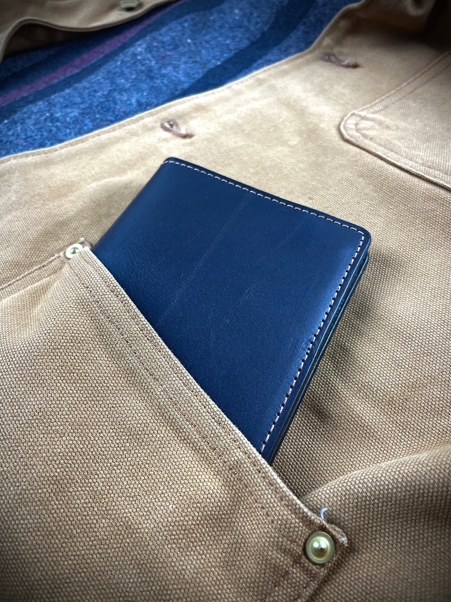 Navy Field Notes cover tucked into the chest pocket of a beige waxed canvas jacket.
