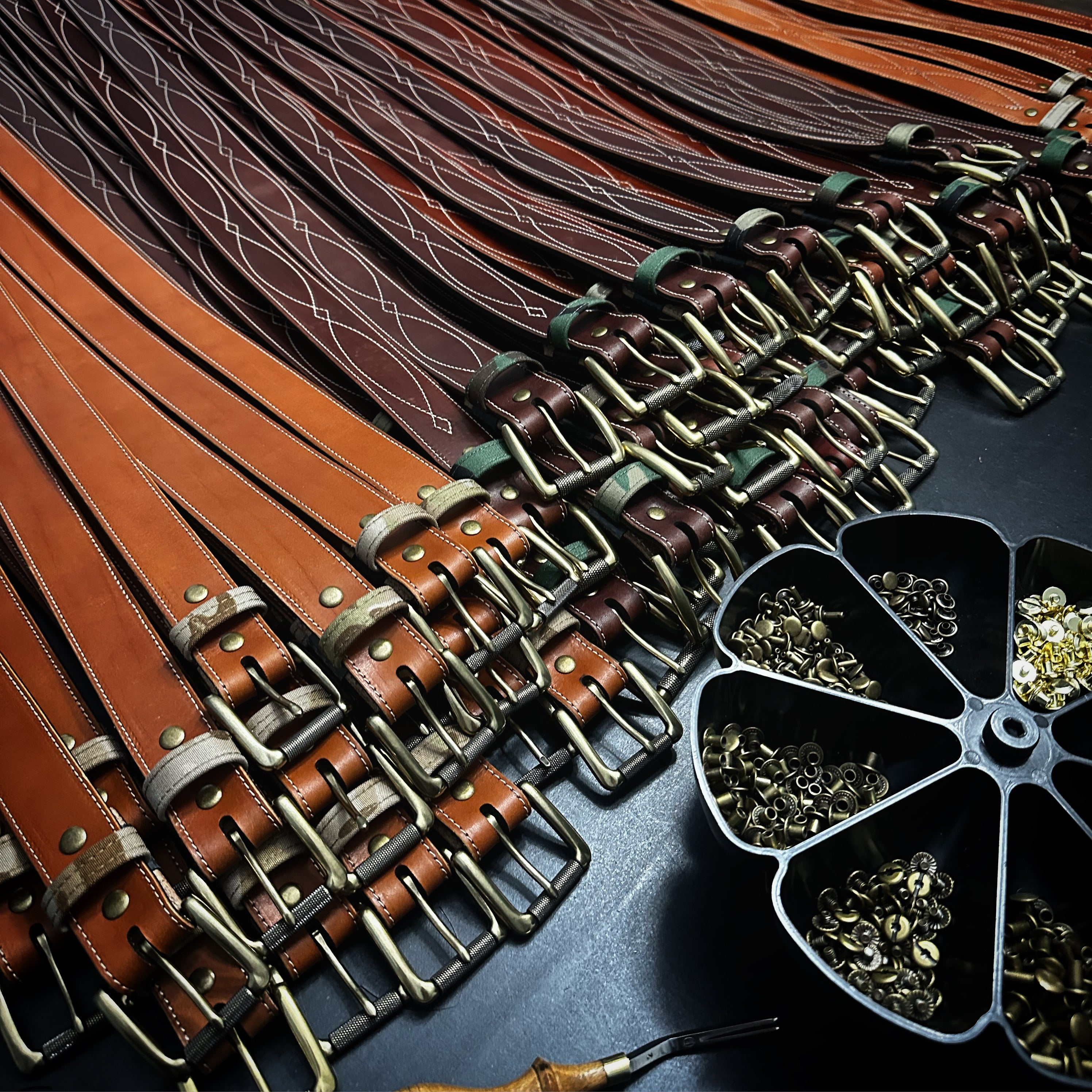 Bulk handcrafted leather belts and brass hardware laid out for large-scale production at Gunnar & Co.