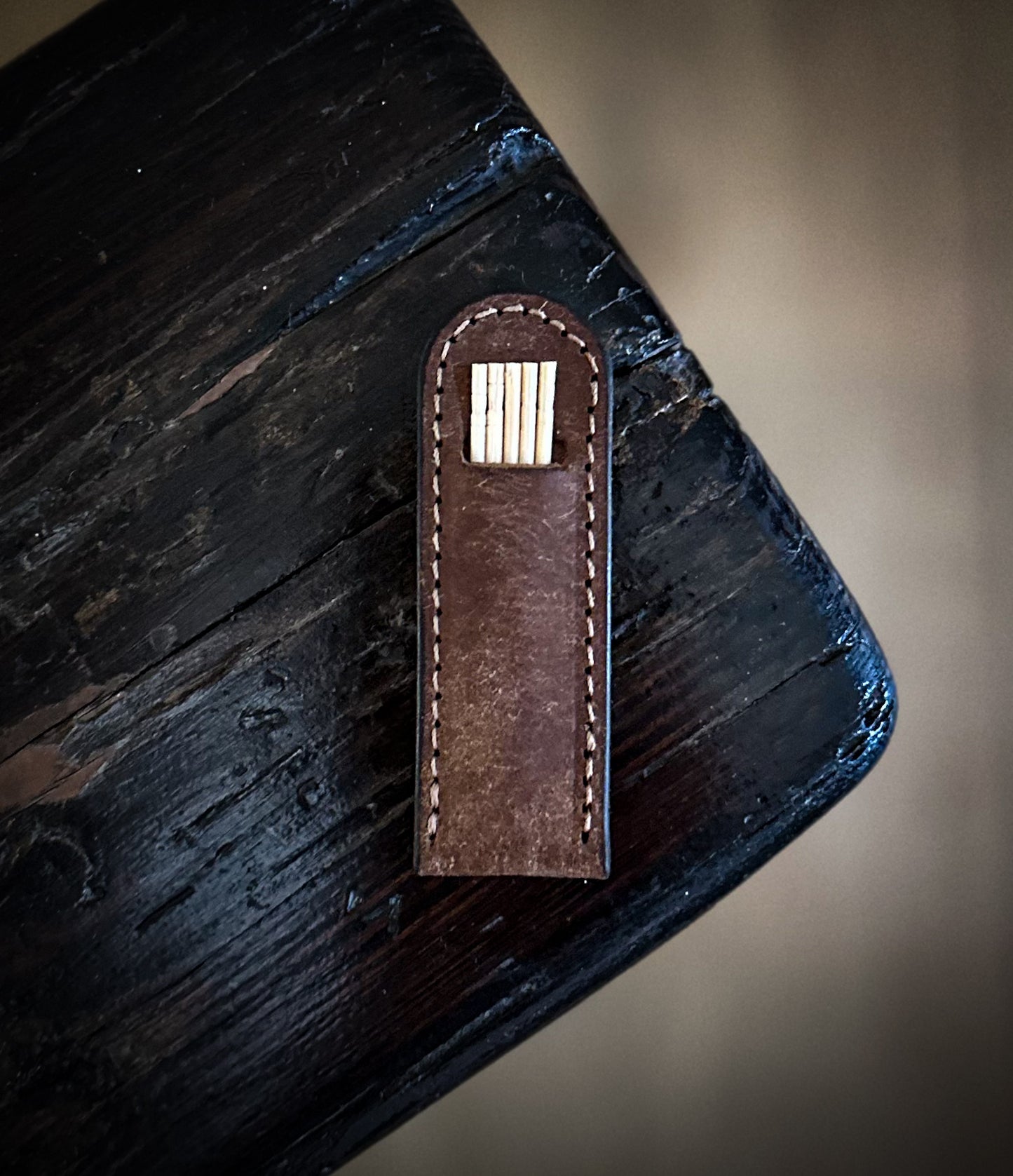 Dark brown leather toothpick holder placed diagonally on dark wood