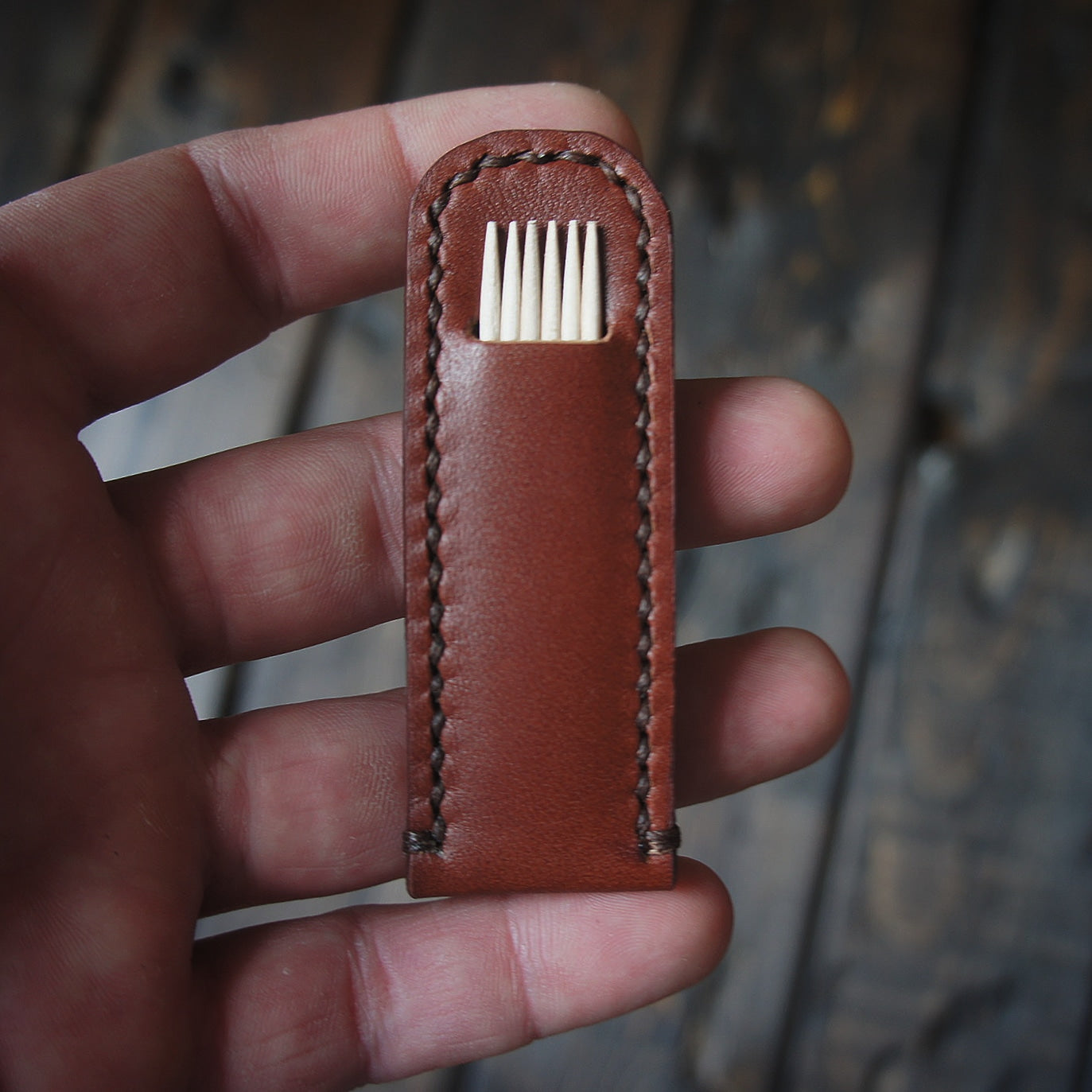 Reddish-brown leather toothpick holder held in hand with visible toothpicks